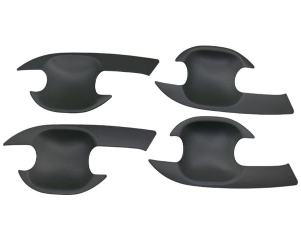 Four black, curved, plastic car door handle covers are positioned symmetrically on a plain background. They have an ergonomic design with cutouts for easy installation.