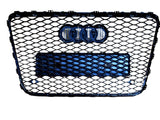 A black honeycomb car grille with the Audi logo prominently displayed, featuring four interlocking rings. The grille is set against a plain white background.