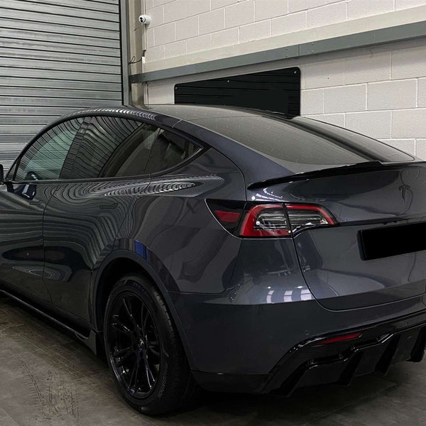 A sleek, dark-colored car is parked in a garage beside a metallic shutter. The car's glossy surface reflects the surroundings.
