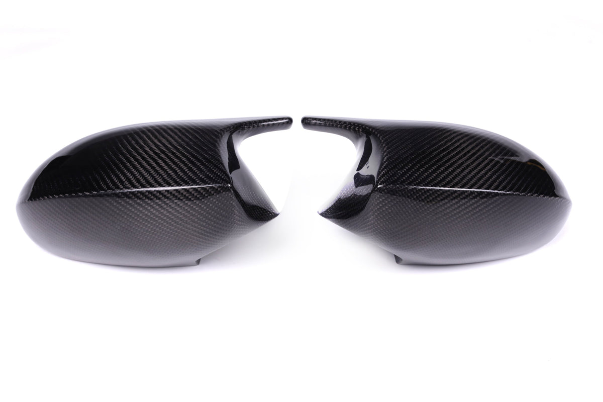 Two carbon fiber car mirror covers face each other against a plain white background, displaying a sleek, glossy surface with a distinct woven pattern.