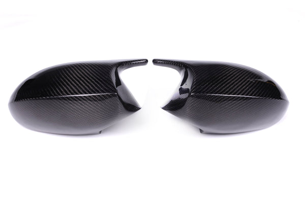 Two carbon fiber car mirror covers face each other against a plain white background, displaying a sleek, glossy surface with a distinct woven pattern.