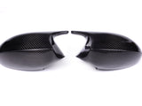 Two black carbon fiber car mirror covers face each other, resting on a plain white background, highlighting their glossy texture and sleek design.