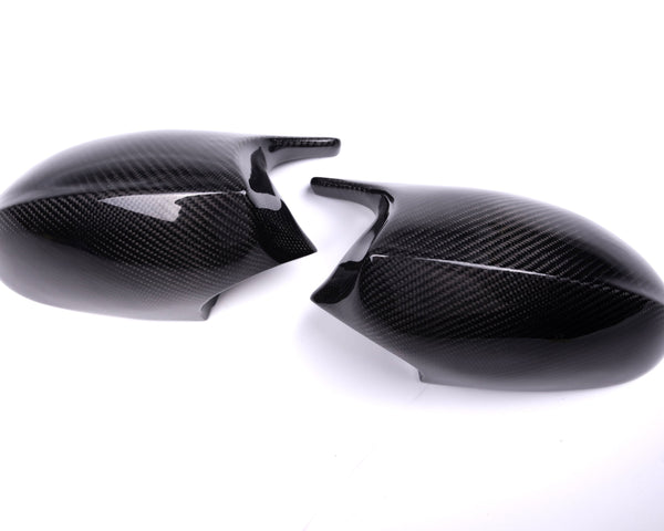 Two carbon fiber mirror caps rest on a white surface, featuring a glossy finish and textured pattern, suggesting use in automotive applications.
