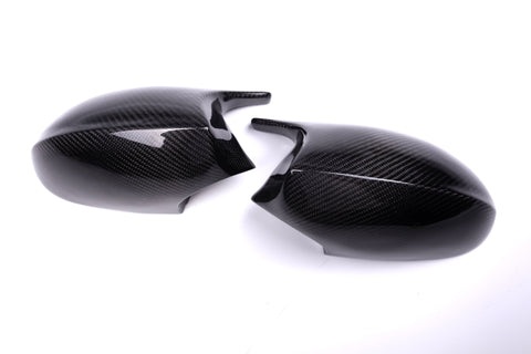 Two carbon fiber mirror caps rest on a white surface, featuring a glossy finish and textured pattern, suggesting use in automotive applications.