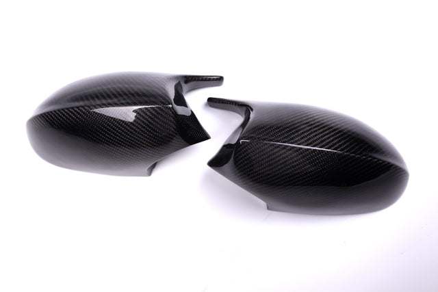 Two carbon fiber mirror caps rest on a white surface, featuring a glossy finish and textured pattern, suggesting use in automotive applications.