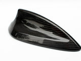 A carbon fiber car antenna is resting on a plain white surface, showcasing a sleek, aerodynamic design with a glossy finish and a subtle checkered pattern.