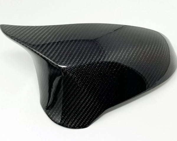 A glossy carbon fiber car mirror cap with a sleek, curved design, rests on a plain white background, showing its textured surface.
