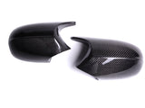 Two glossy carbon fiber mirror covers are placed side by side on a white surface, displaying a sleek, reflective finish and textured pattern.