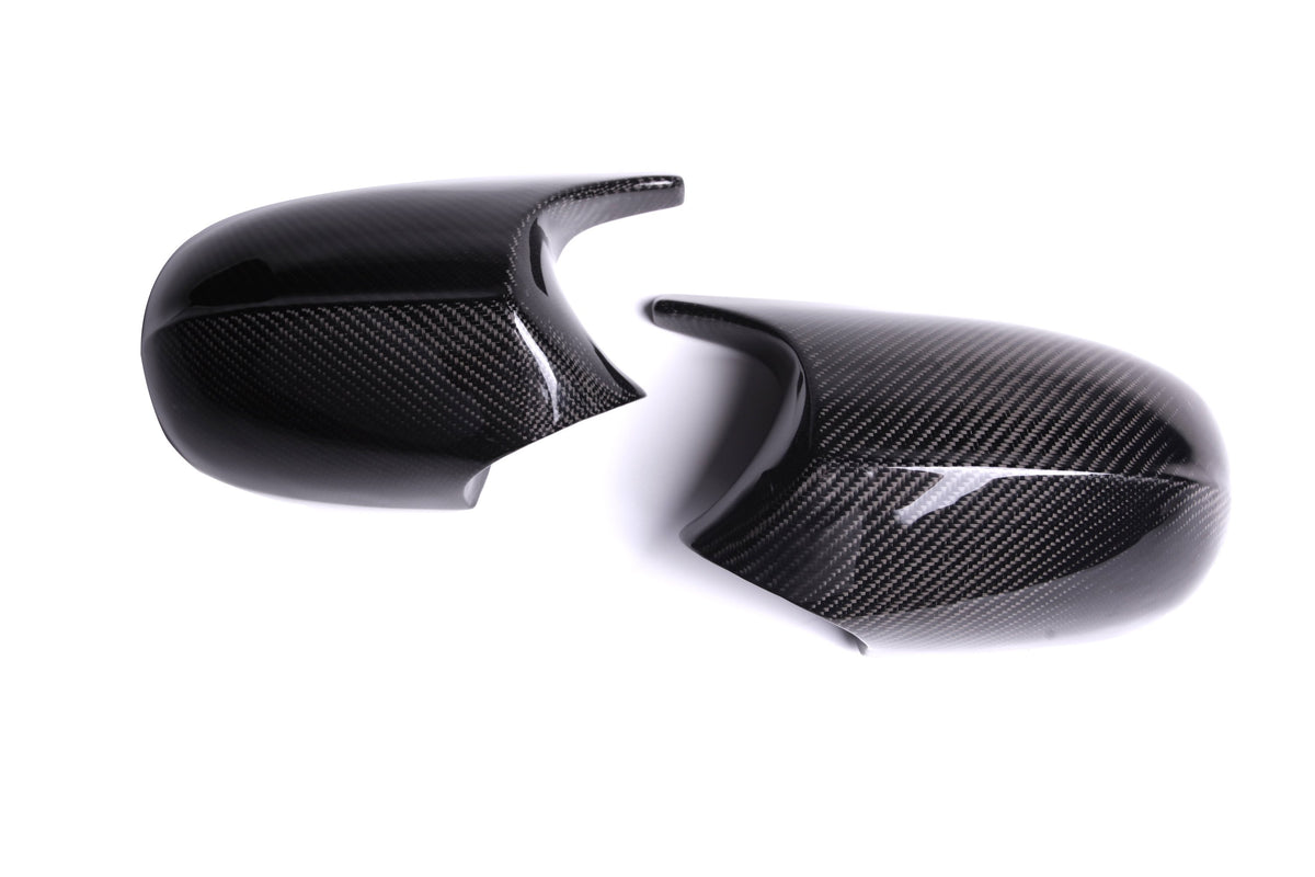 Two glossy carbon fiber mirror covers are placed side by side on a white surface, displaying a sleek, reflective finish and textured pattern.
