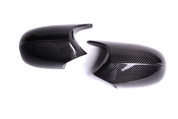 Two glossy carbon fiber mirror covers are placed side by side on a white surface, displaying a sleek, reflective finish and textured pattern.