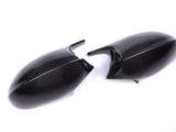 Two carbon fiber car side mirror covers lie on a white surface, displaying a sleek, glossy texture and a subtle weave pattern.