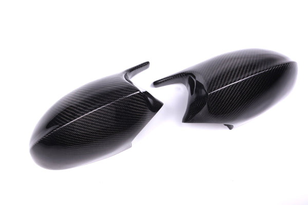 Two carbon fiber car side mirror covers lie on a white surface, displaying a sleek, glossy texture and a subtle weave pattern.