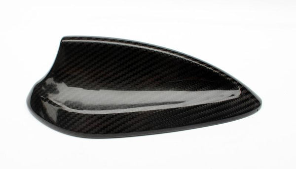 A carbon fiber car side mirror cover resting on a white background, showcasing a glossy finish and textured pattern, highlighting its sleek design and lightweight material.