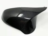 A glossy, black carbon fiber car mirror cover rests on a plain white background, its surface reflecting light with a distinctive woven pattern.