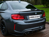 A dark gray BMW sports car is parked on a wet road, featuring a dual exhaust and distinctive rear lights, with a license plate reading 