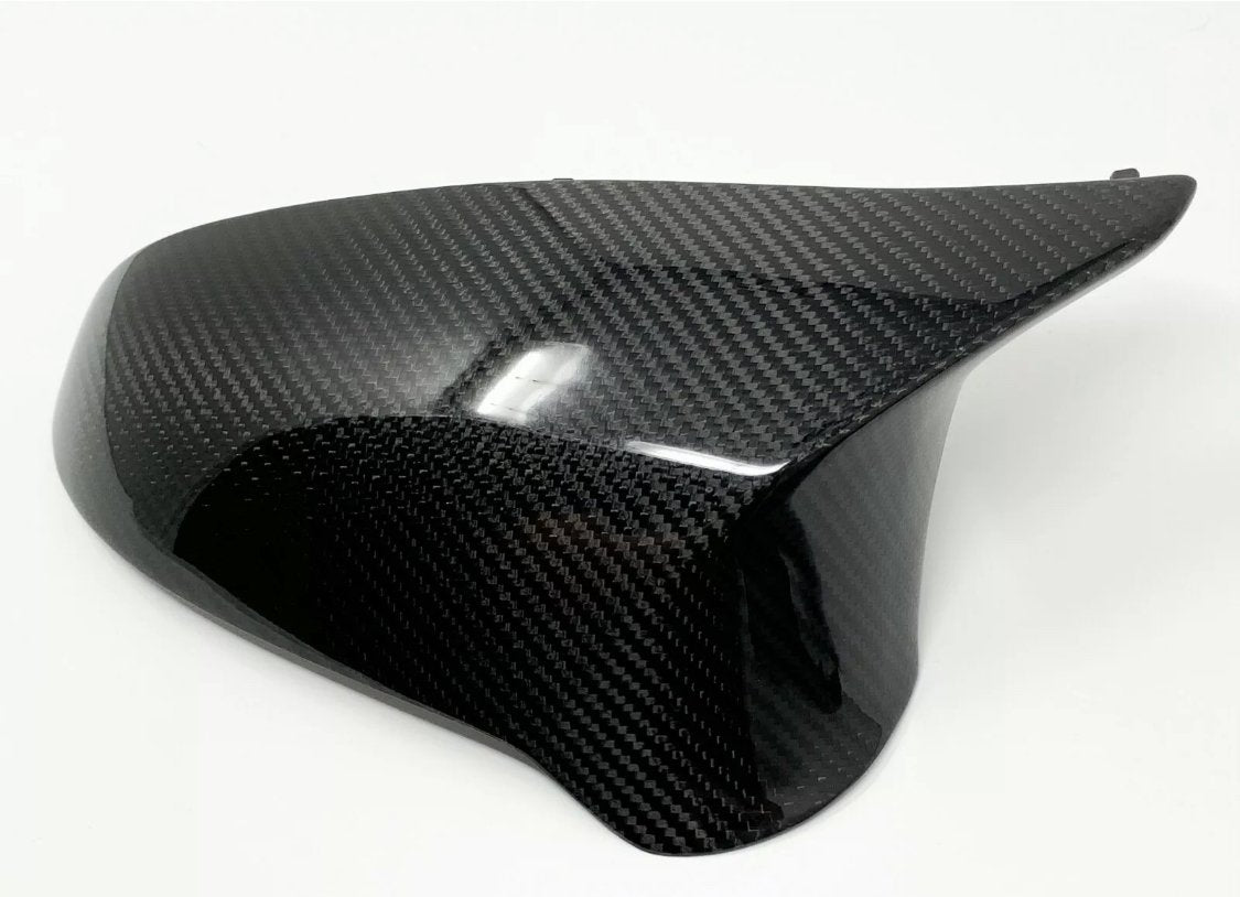 A smooth, black carbon fiber car mirror cover with a glossy finish is resting on a plain white surface, highlighting its sleek design and reflective texture.