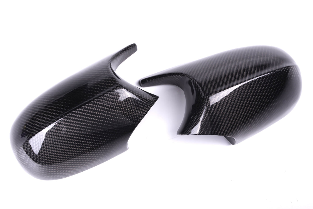 Two black carbon fiber car side mirror covers lie adjacent on a white surface, showcasing their glossy texture and sleek, aerodynamic shape.