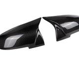 Two glossy carbon fiber side mirror covers rest adjacent, reflecting light and featuring a distinct weaved pattern; placed against a plain white background.