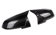 Two glossy carbon fiber side mirror covers rest adjacent, reflecting light and featuring a distinct weaved pattern; placed against a plain white background.