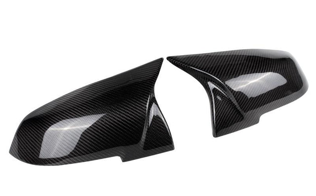 Two glossy carbon fiber side mirror covers rest adjacent, reflecting light and featuring a distinct weaved pattern; placed against a plain white background.