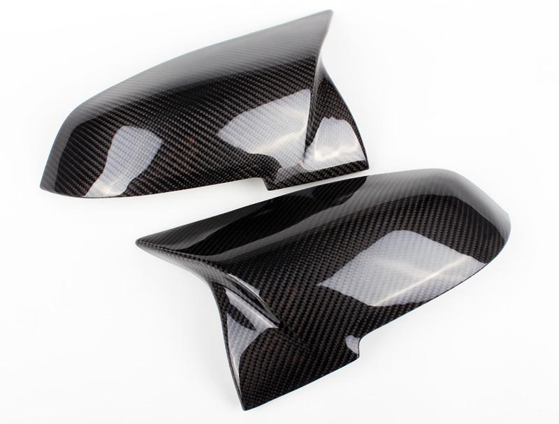 Two glossy carbon fiber side mirror covers rest on a clean white surface, showcasing their sleek, aerodynamic design.