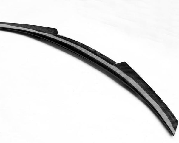 Carbon fiber car spoiler rests on a plain white surface. Its smooth, sleek design features a curved, aerodynamic shape, highlighting its purpose in enhancing vehicle performance and appearance.