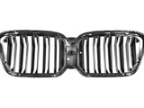 A shiny, black car grille with vertical slats is isolated on a white background. It features a dual-kidney design and has small text and markings visible on the connecting center bar.