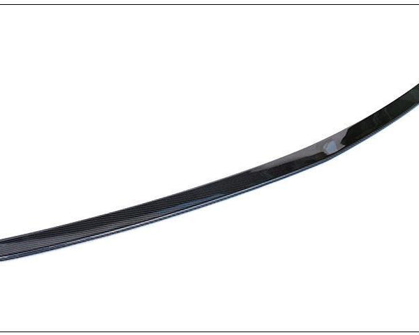 A sleek, curved carbon fiber spoiler lies on a plain white background. The spoiler's glossy surface reflects light, highlighting its aerodynamic design.