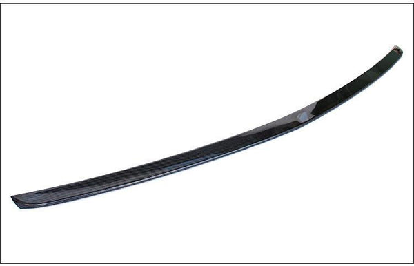 A sleek, curved carbon fiber spoiler lies on a plain white background. The spoiler's glossy surface reflects light, highlighting its aerodynamic design.