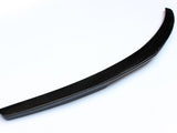A curved, black carbon fiber car spoiler rests on a white surface, showcasing its sleek, aerodynamic design.