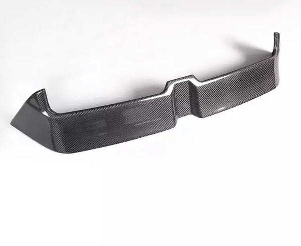 A carbon fiber car bumper sits on a white background, showcasing a sleek, angular design with a textured surface and raised edges.