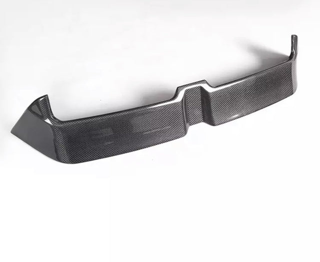 A carbon fiber car bumper sits on a white background, showcasing a sleek, angular design with a textured surface and raised edges.