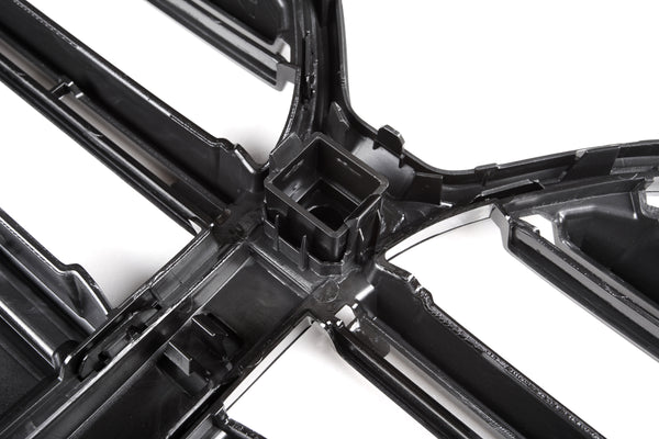 A black plastic grid structure sits on a white background, featuring intersecting lines with a central square cavity, likely part of an automotive or industrial component.