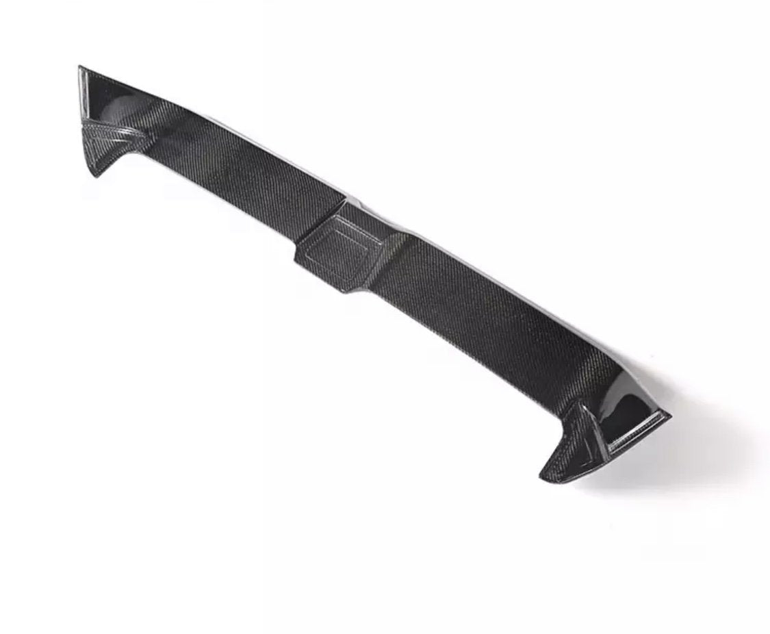 A carbon fiber car spoiler lies on a plain white background, highlighting its aerodynamic shape and texture.