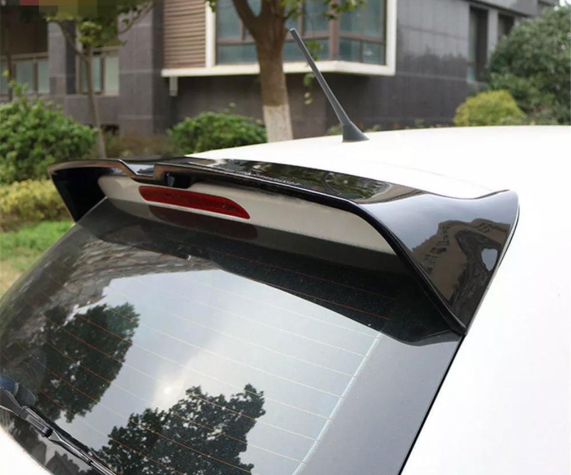 A car rear end with a spoiler and antenna is parked outdoors near a building, surrounded by greenery and trees. Reflections are visible on the rear window.
