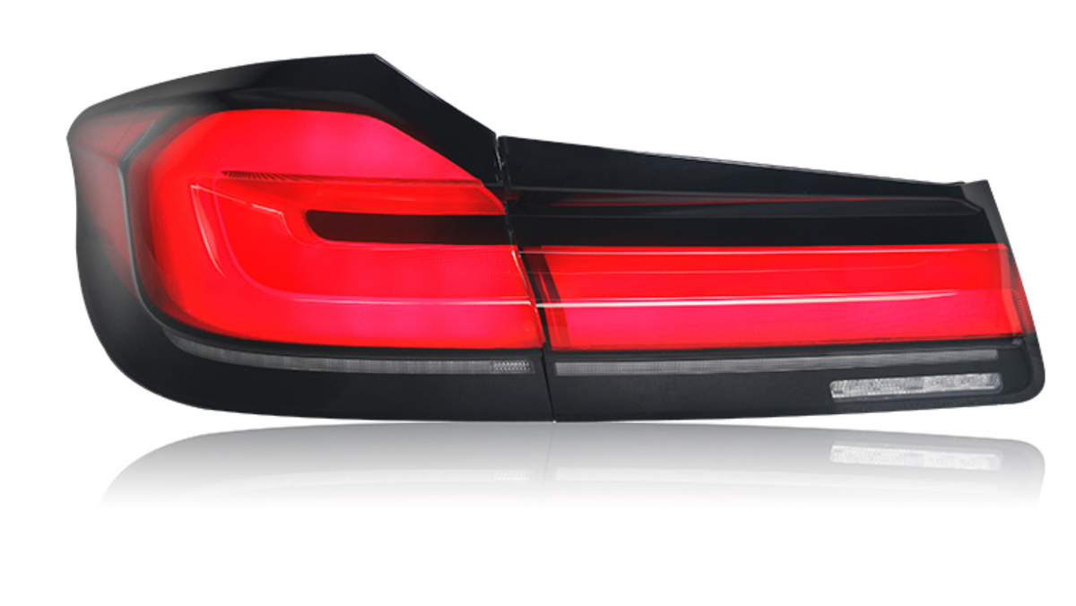 A red car taillight is illuminated, displaying sleek horizontal lines. It is isolated against a white background, highlighting the light's modern design and glossy finish.
