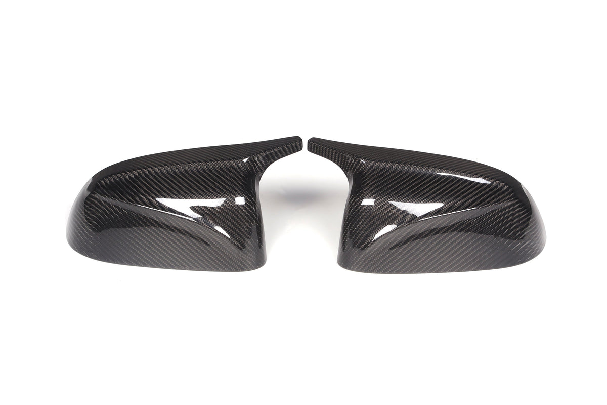 Two carbon fiber side mirror covers are positioned side by side, slightly angled inward, on a plain white background, showcasing their glossy, textured surfaces.