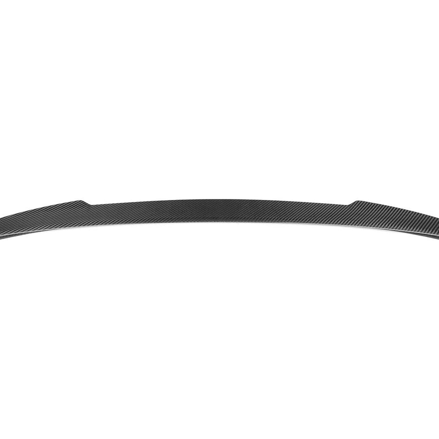 A sleek, curved carbon fiber spoiler rests against a plain white background, showcasing its streamlined design and subtle patterning ideal for automotive aerodynamic enhancement.