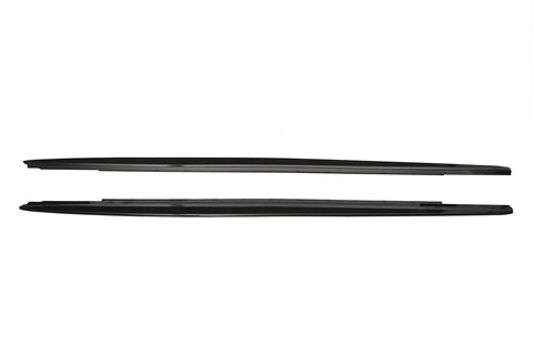 Two sleek, black car side skirts, aligned horizontally, lie against a plain white background, showing their aerodynamic design and smooth edges.