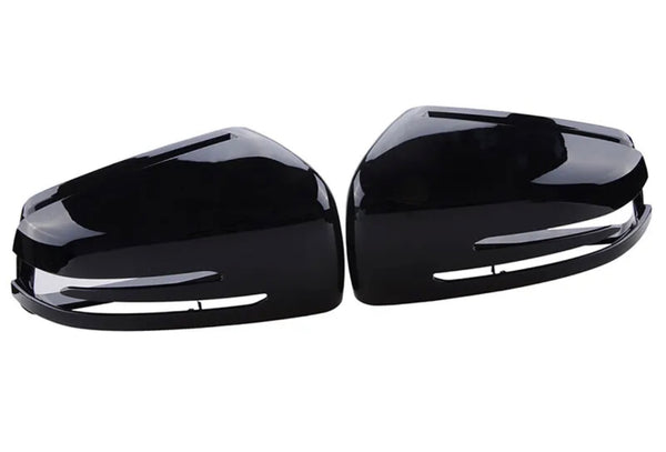 Glossy black car side mirror covers lie face up, displaying their sleek, aerodynamic shape. Positioned parallel to each other, they rest on a white, featureless background.