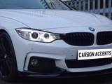 A white BMW car with illuminated headlights and black wheels is parked beside a metal fence. The license plate reads 