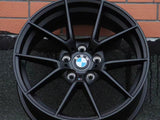 A black BMW car wheel rim with a logo at the center is leaning against a brick wall on a textured ground surface.