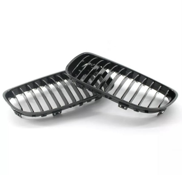 Two black car grilles rest on a white surface, showcasing their shiny, vertical slats and curved rectangular frames, designed for vehicle front-end placement.