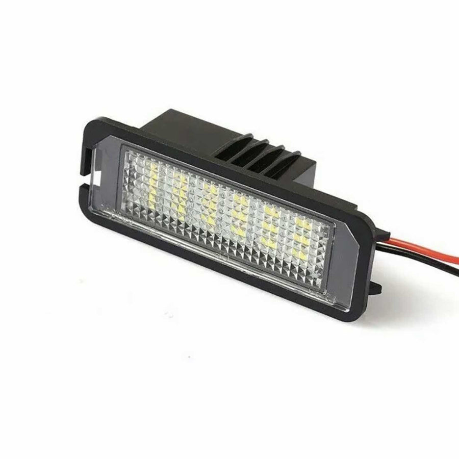 A rectangular LED light with a black housing and transparent cover sits on a white surface. Red and black wires extend from its rear, indicating connectivity features.