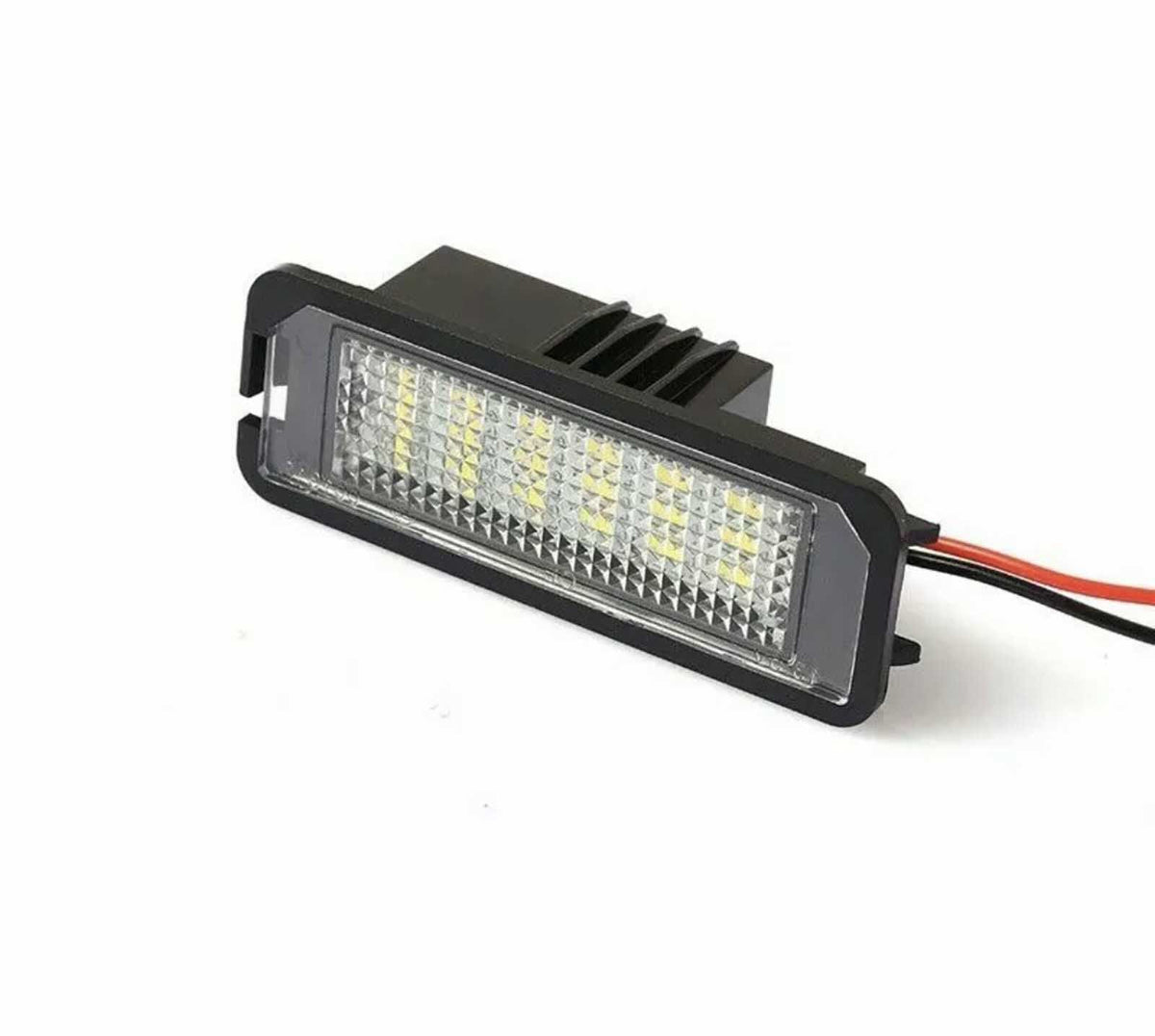 A rectangular LED light with a black housing and clear, textured lens is illuminated, featuring yellow diodes. It has red and black wires extending from the back, set against a plain background.