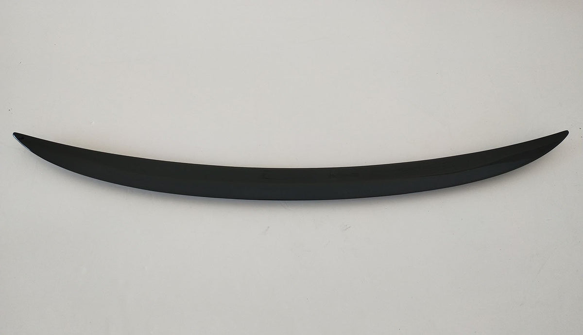 A curved, sleek, black object rests horizontally on a plain, light-colored background, resembling a minimalist sculpture or car spoiler.