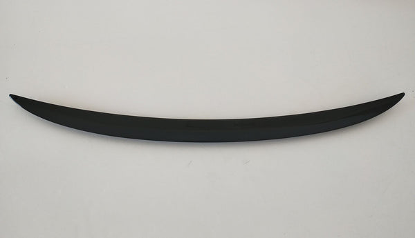 A curved, sleek, black object rests horizontally on a plain, light-colored background, resembling a minimalist sculpture or car spoiler.