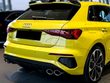 A yellow Audi car is parked in a showroom, showcasing a sporty rear design with dual exhausts under bright lighting. A black license plate covers the rear branding.