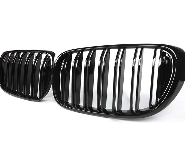 Two glossy black car grilles with vertical slats are displayed against a plain white background. The design suggests modern automotive styling.