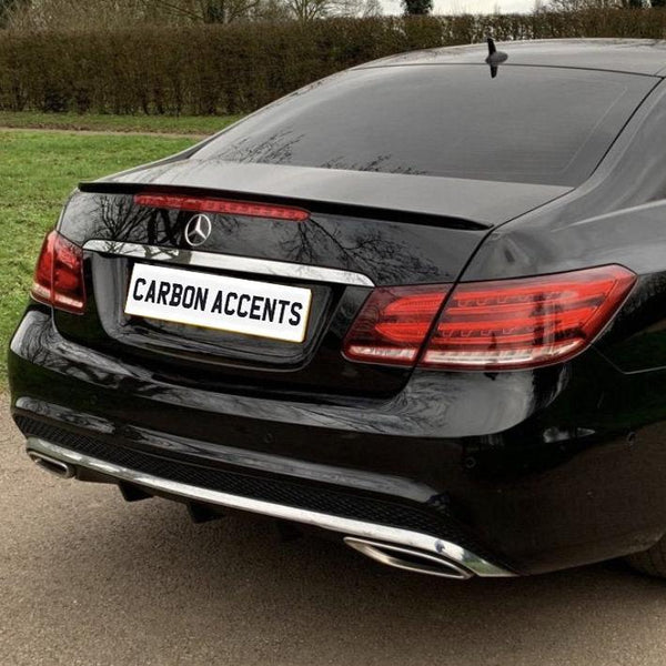 A black car with a "CARBON ACCENTS" license plate is parked on a paved road, surrounded by grass and trees in the background.